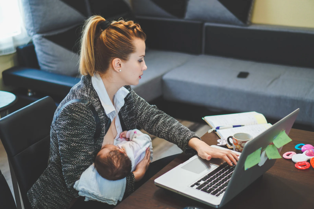 Maman travaillant sur son ordinateur portable avec son bébé dans les bras